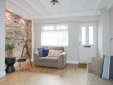 A living room with two sofas pillows a stone feature wall a tripod lamp and a white front door with windows at Ty Bara in Cemaes Bay