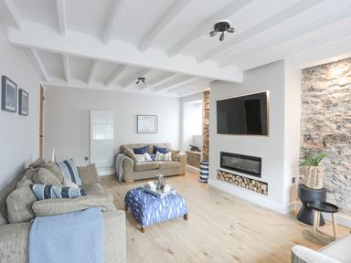 A living room with two sofas a blue patterned ottoman a wall mounted television and fireplace at Ty Bara in Cemaes Bay