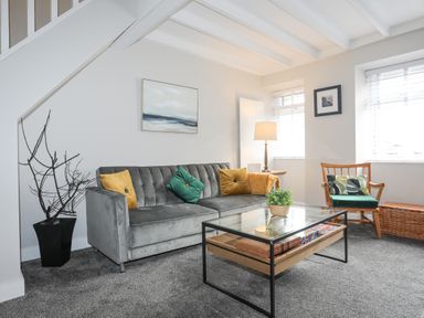 A living room with a gray sofa with cushions a glass coffee table a wooden chair and windows with blinds at Ty Bara in Cemaes Bay
