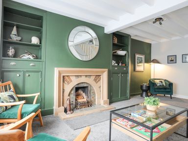 A living room with a green fireplace wall wooden chairs a glass coffee table and a green armchair at Ty Bara in Cemaes Bay
