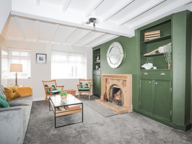 A living room with a green built-in cabinet and fireplace a sofa armchairs and a glass coffee table at Ty Bara in Cemaes Bay