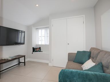 A living room with a wall-mounted TV a bench a window with blinds and a sofa with cushions at Ty Bara in Cemaes Bay