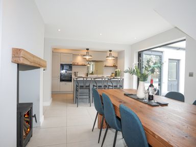 A kitchen with an island and bar stools next to a dining table with chairs and a vase of flowers at Ty Bara in Cemaes Bay