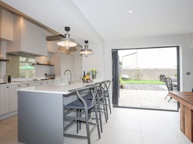 A kitchen with an island and bar stools next to an open patio door leading to a garden at Ty Bara in Cemaes Bay