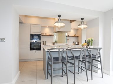 A kitchen with an island and three stools under pendant lights at Ty Bara in Cemaes Bay