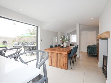A dining room with a wooden table and blue chairs next to a sliding glass door leading to a patio at Ty Bara in Cemaes Bay