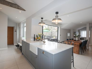A kitchen island with a sink and chairs next to a wooden dining table with chairs at Ty Bara in Cemaes Bay