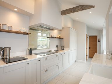 A kitchen with white cabinets wooden shelves and a wooden door at Ty Bara in Cemaes Bay