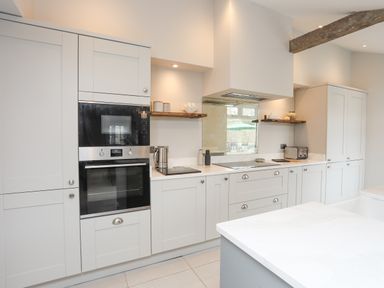 A kitchen with white cabinets built in ovens stovetop kettle toaster and shelves with items at Ty Bara in Cemaes Bay