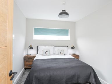 A bedroom with a double bed two bedside tables with lamps and a window with a blue blind at Ty Bara in Cemaes Bay