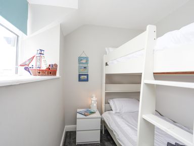 A bedroom with white bunk beds a white nightstand with books and a lighthouse lamp a toy ship on the window sill and three small framed pictures on the wall at Ty Bara in Cemaes Bay
