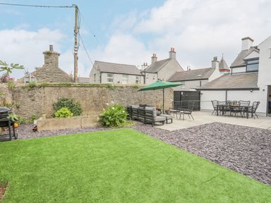 A backyard with grass, patio furniture, an umbrella, and stone walls at Ty Bara in Cemaes Bay