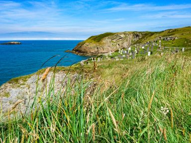A coastal cliff with grass and a cemetery overlooking the ocean at Ty Bara in Cemaes Bay