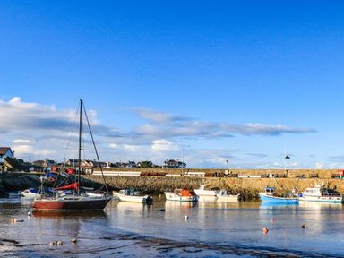 Boats moored in a harbor with a stone wall and houses in the background at Ty Bara in Cemaes Bay