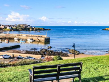 A bench on grass overlooking a harbor with boats and houses near the sea at Ty Bara in Cemaes Bay