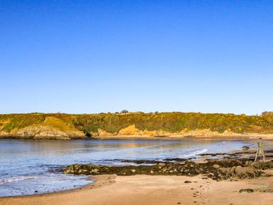 A beach with sand rocks and a hillside in the background at Ty Bara in Cemaes Bay