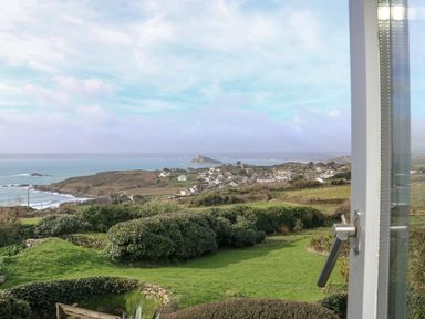 A coastal village with green fields and ocean view seen through a window at An Skyber in Perranuthnoe