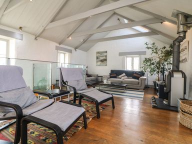 A living room with two armchairs a wood stove a gray sofa and a large plant at An Skyber in Perranuthnoe