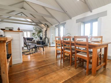 A dining area with a wooden table and chairs next to a living room with seating and a wood stove at An Skyber in Perranuthnoe