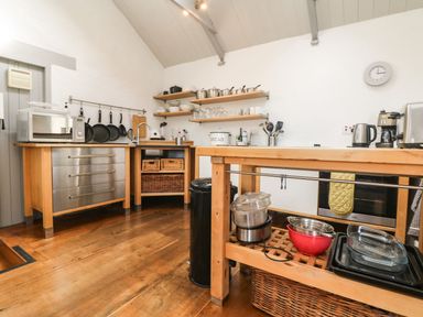 A kitchen with wooden cabinets metal drawers hanging pans open shelves with dishes and a wooden island with kitchen appliances at An Skyber in Perranuthnoe