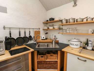 A kitchen corner with a sink hanging pans pots and glassware on shelves at An Skyber in Perranuthnoe
