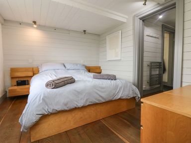 A bedroom with a bed, striped bedding, wooden side tables, a chest of drawers, and a doorway at An Skyber in Perranuthnoe