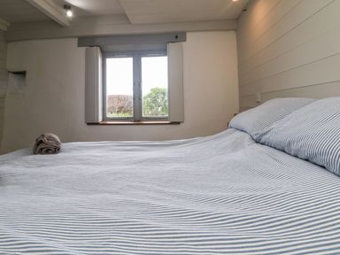 A bedroom with a double bed striped bed linen and a window with shutters at An Skyber in Perranuthnoe