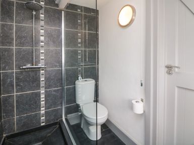 A bathroom with a shower area with dark tiles a toilet and a wall light at An Skyber in Perranuthnoe