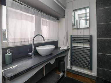 A bathroom sink with a faucet soap dispenser and a towel on the counter a mirror and a heated towel rail on the wall at An Skyber in Perranuthnoe