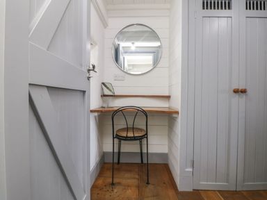 A small corner with a wooden desk chair a round wall mirror and a small mirror on the desk at An Skyber in Perranuthnoe