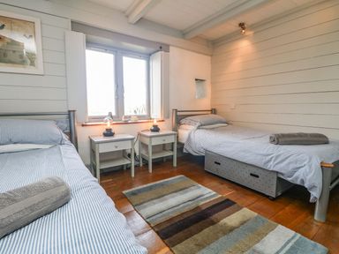 A bedroom with two single beds bedside tables with lamps striped bedding and a striped rug on wooden floor at An Skyber in Perranuthnoe