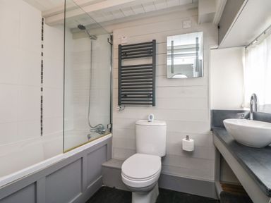 A bathroom with a bathtub and showerhead a toilet a wall-mounted heated towel rail a mirror and a sink on a countertop at An Skyber in Perranuthnoe