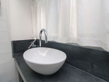 A bathroom sink with a round white basin and a chrome faucet on a dark countertop at An Skyber in Perranuthnoe