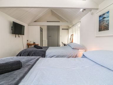 A bedroom with two beds striped bedding a TV on the wall and a dressing table at An Skyber in Perranuthnoe