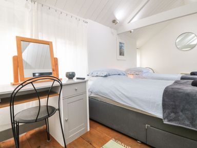 A bedroom with two single beds a desk with a mirror and a metal chair at An Skyber in Perranuthnoe