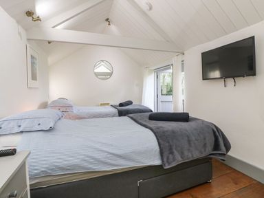 A bedroom with two single beds a wall-mounted television and a door with curtains at An Skyber in Perranuthnoe