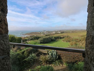 A coastal landscape with green fields and a garden seen from a stone window at An Skyber in Perranuthnoe