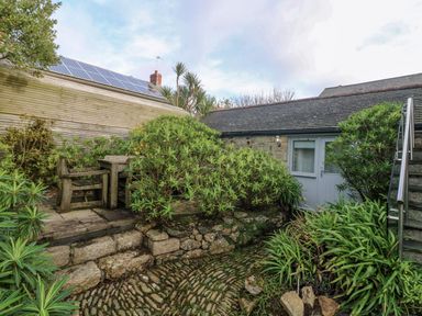 An outdoor garden area with stone steps wooden bench and table surrounded by plants at An Skyber in Perranuthnoe