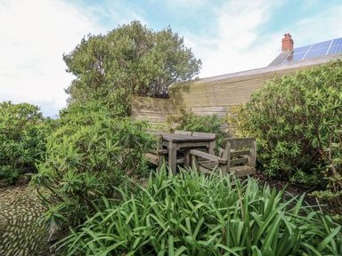 An outdoor seating area with wooden furniture surrounded by green plants and a wooden fence at An Skyber in Perranuthnoe
