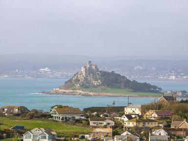 A coastal village with houses and an island with a castle in the sea at An Skyber in Perranuthnoe