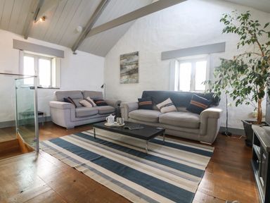 A living room with two sofas pillows coffee table striped rug and a large plant at An Skyber in Perranuthnoe