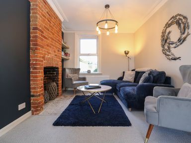 A living room with a brick fireplace a blue rug and grey and blue seating at First Light in Pakefield near Lowestoft