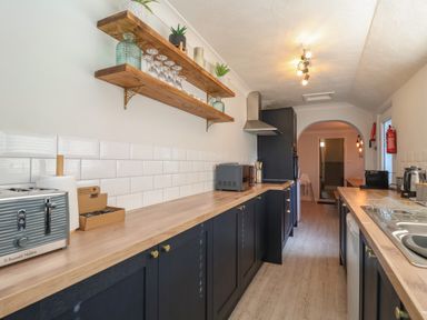A galley kitchen with wooden countertops open shelves with glassware and plants and appliances at First Light in Pakefield near Lowestoft