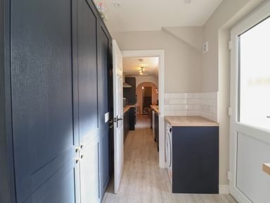 A narrow kitchen with dark cabinets a washing machine and wooden countertops at First Light in Pakefield near Lowestoft