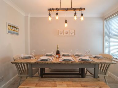 A dining room with a wooden table set for eight with plates glasses and a bottle under hanging light at First Light in Pakefield near Lowestoft