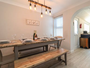 A dining area with a wooden table set with plates and glasses and a bench and chairs at First Light in Pakefield near Lowestoft