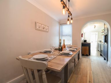A dining area with a wooden table set for six and a kitchen visible through an archway at First Light in Pakefield near Lowestoft