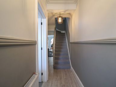 A narrow hallway with stairs ahead a door on the left and a hanging light at First Light in Pakefield near Lowestoft