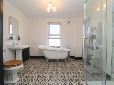 A bathroom with a toilet a sink a freestanding bathtub a glass shower and a shelving unit at First Light in Pakefield near Lowestoft