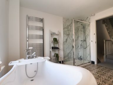 A bathroom with a bathtub shower cubicle towel rack and shelving unit at First Light in Pakefield near Lowestoft